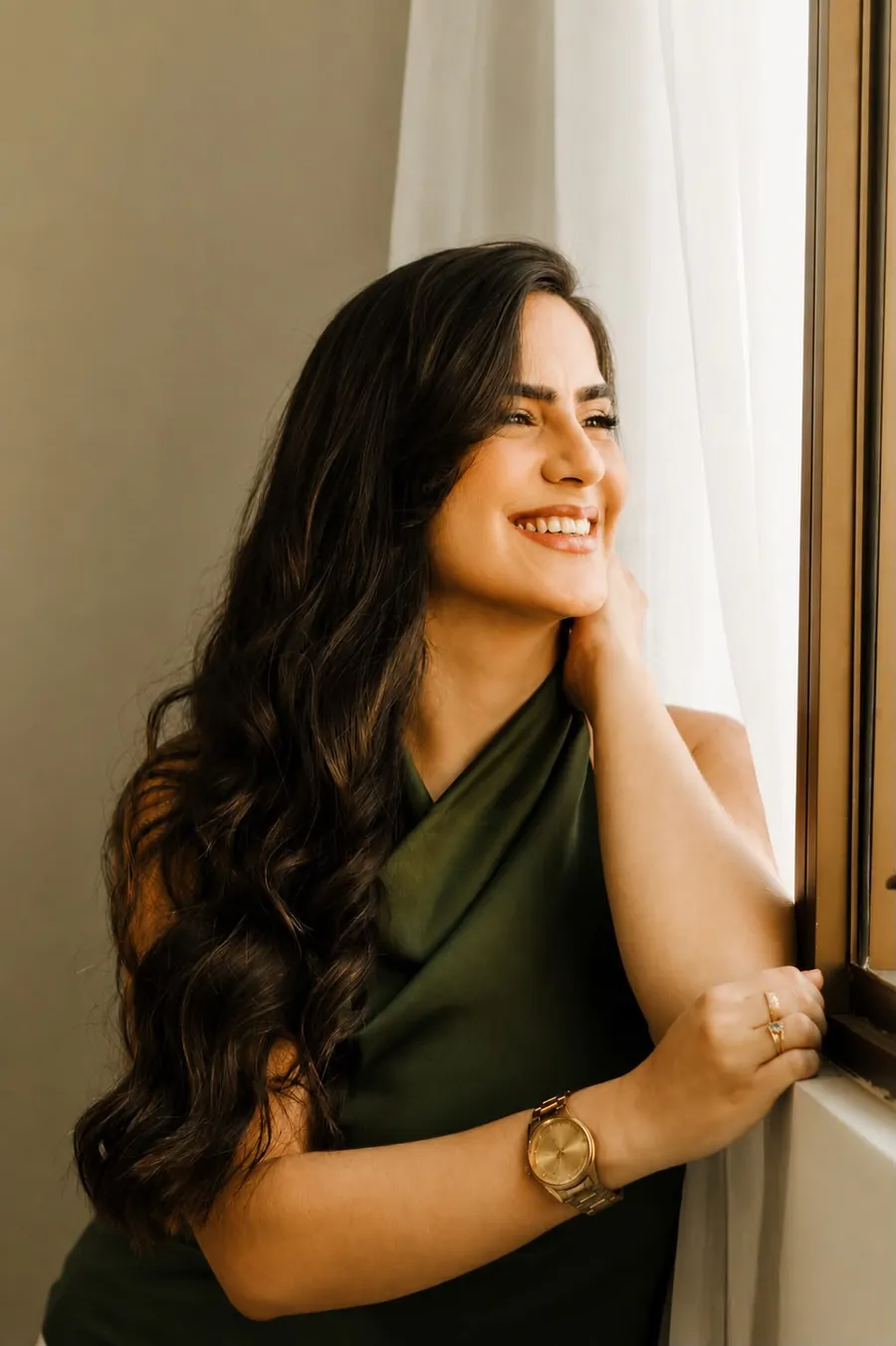Raissa Macedo sorrindo ao lado da janela, de blusa de cetim verde
