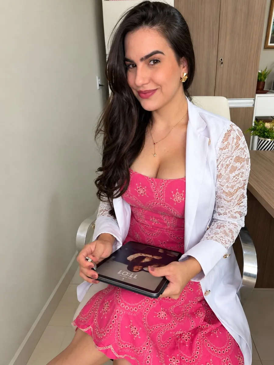 Raissa Macedo de vestido rosa e jaleco branco, sorrindo e segurando um tablet